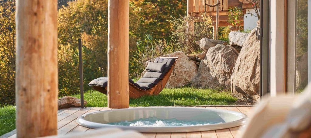 Luxus-Chalet Terrasse mit eingelassenem Whirlpool, rustikalen Holzbalken und natürlicher Feldstein-Mauer im herbstlichen Garten.