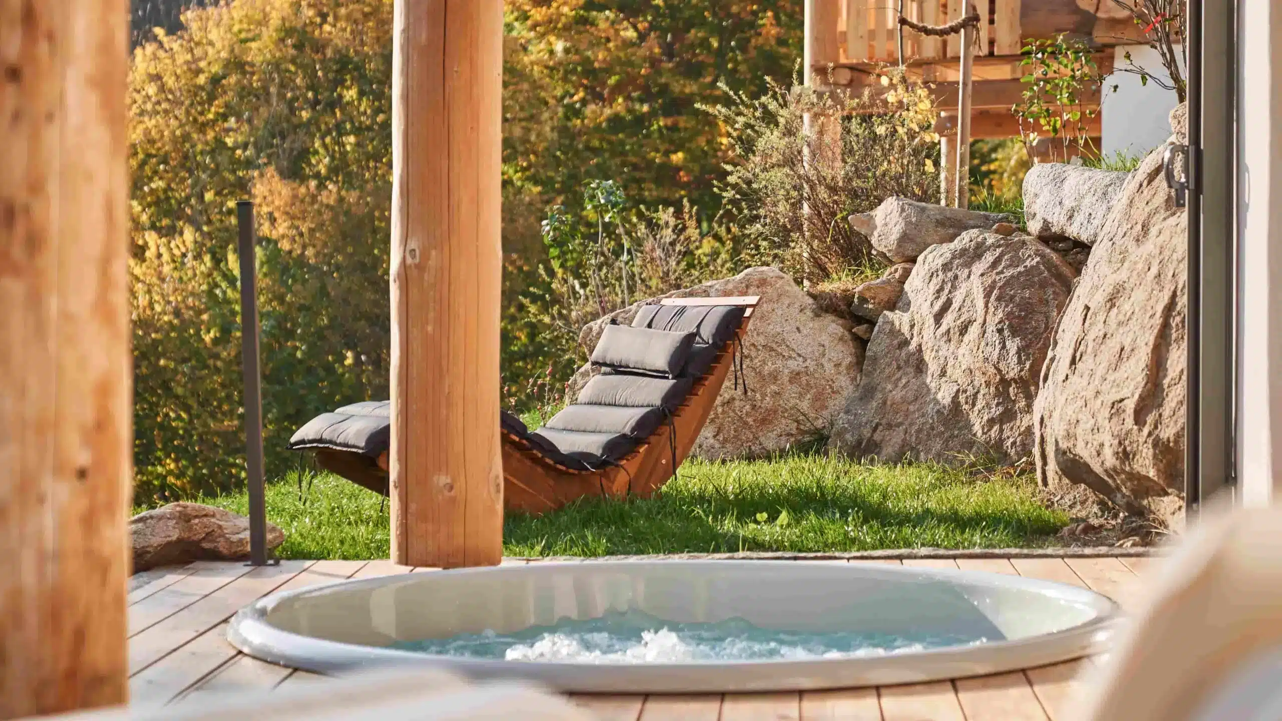 Luxus-Chalet Terrasse mit eingelassenem Whirlpool, rustikalen Holzbalken und natürlicher Feldstein-Mauer im herbstlichen Garten