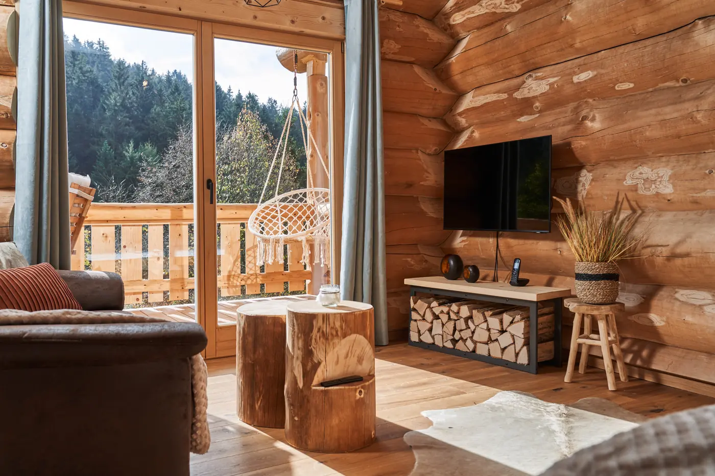 Wohnbereich des Chalets Fichtenstamm mit Sofa, Fernseher und Glastür zum Balkon