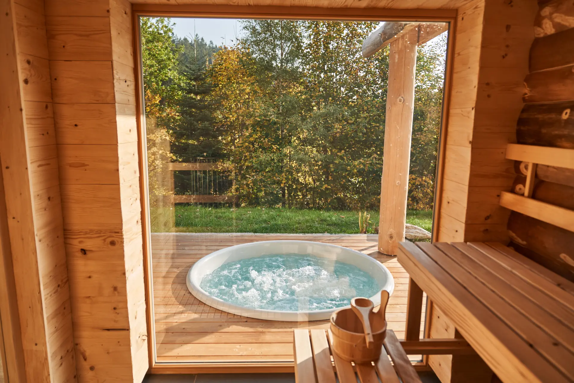Blick aus der privaten Sauna durch ein großes Fenster auf den Whirlpool im Garten